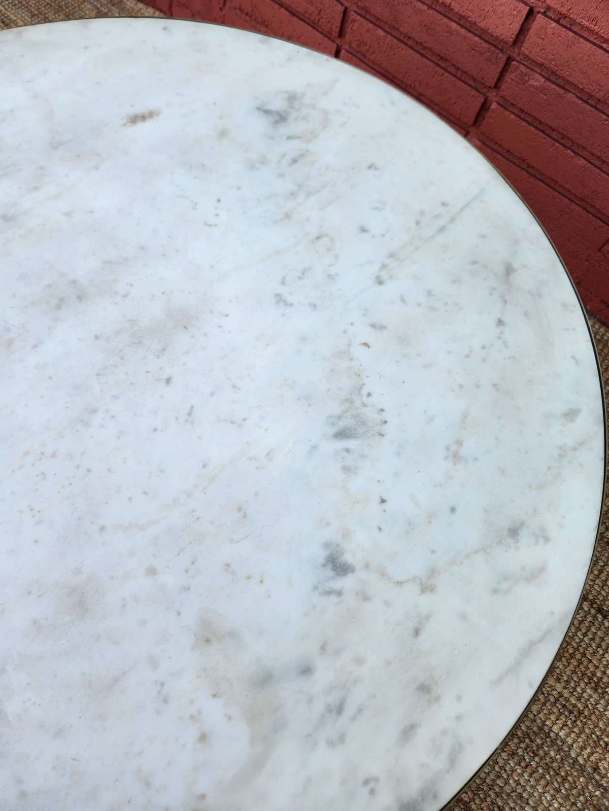Closeup of a round white marble tabletop with gray veining, placed on a beige rug next to red cushioned furniture