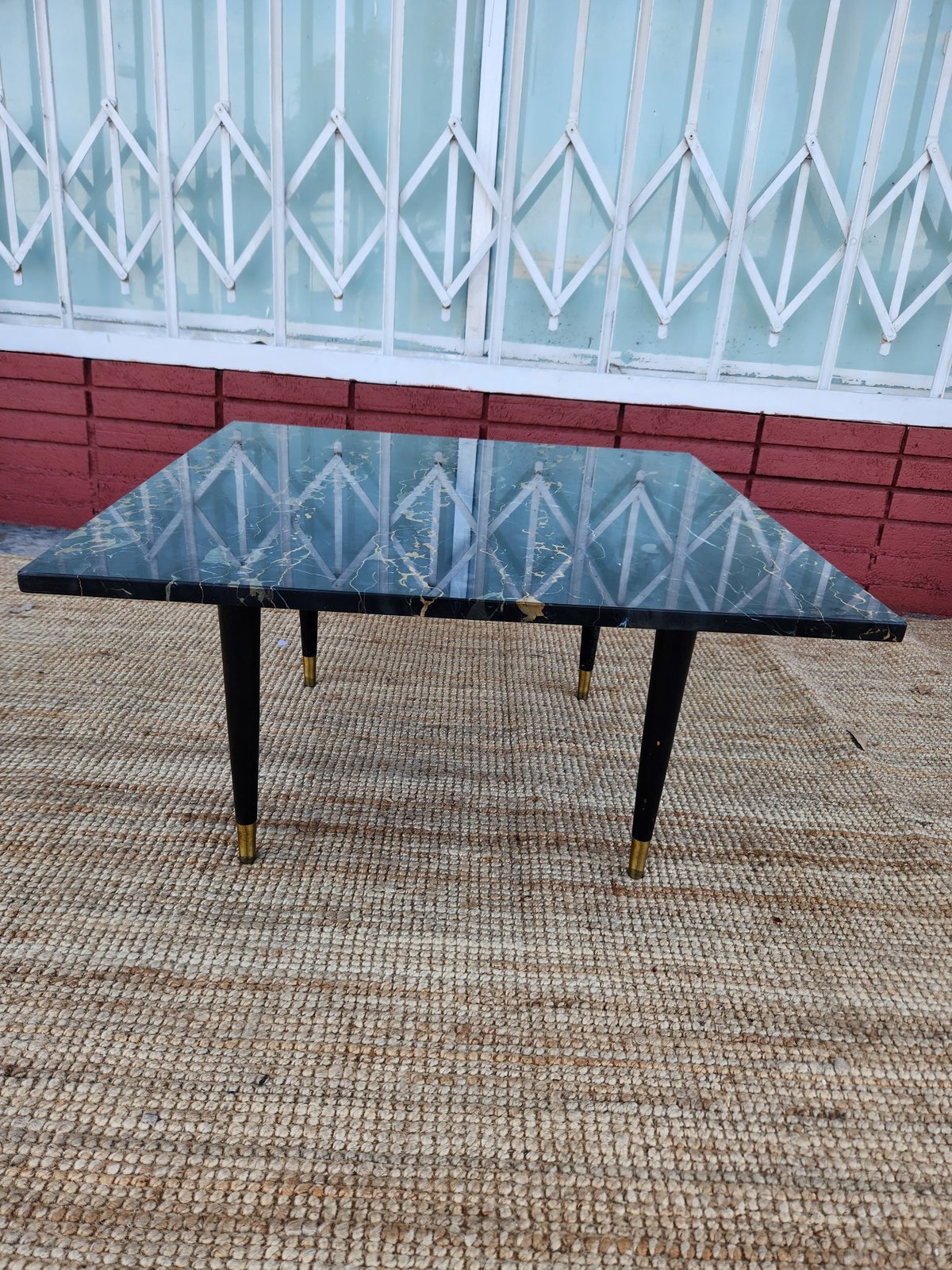 Black mid-century modern coffee table with tapered legs displayed outdoors on a concrete patio