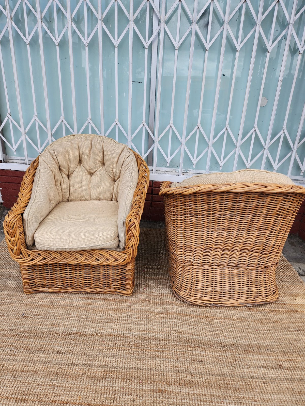Wicker armchair with cream cushion beside a wicker side table against a metal corrugated wall
