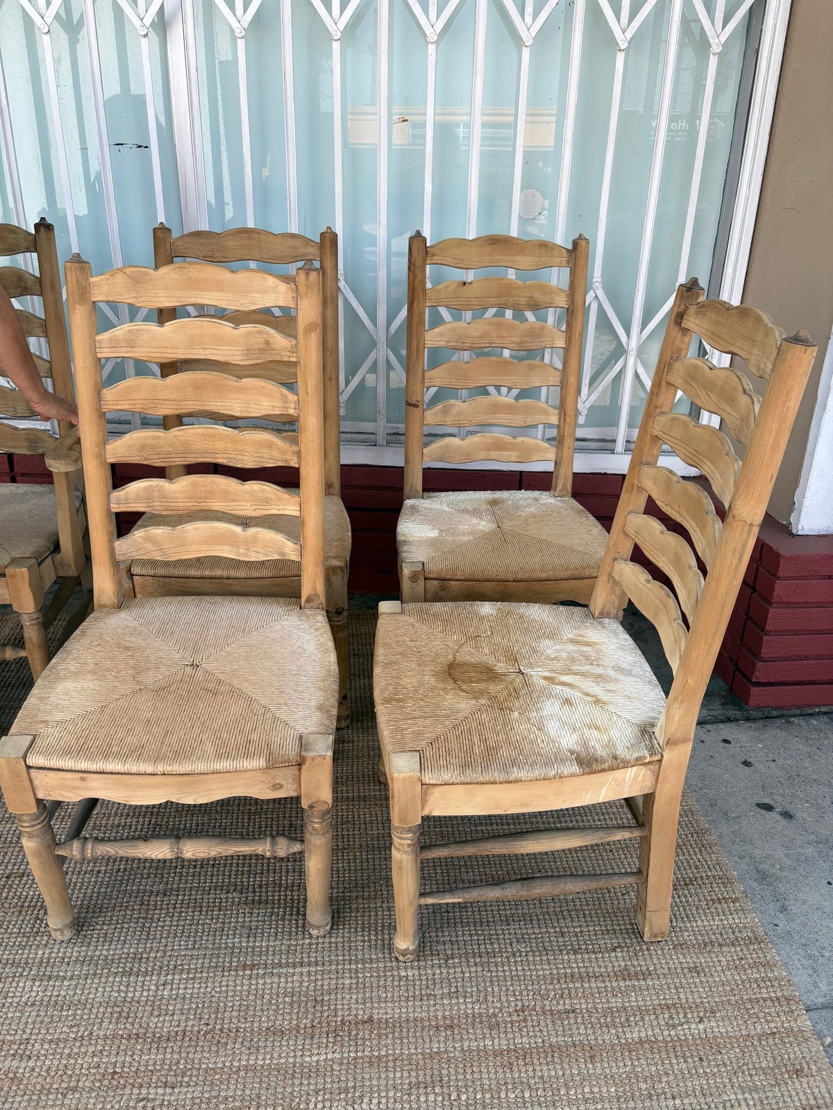 Wooden dining chairs with woven rush seats arranged in a row against a window with sheer curtains indoors