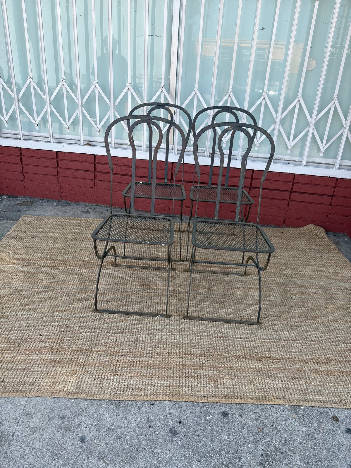 Metal patio dining set with two chairs and a table on a woven mat against a red and white wall