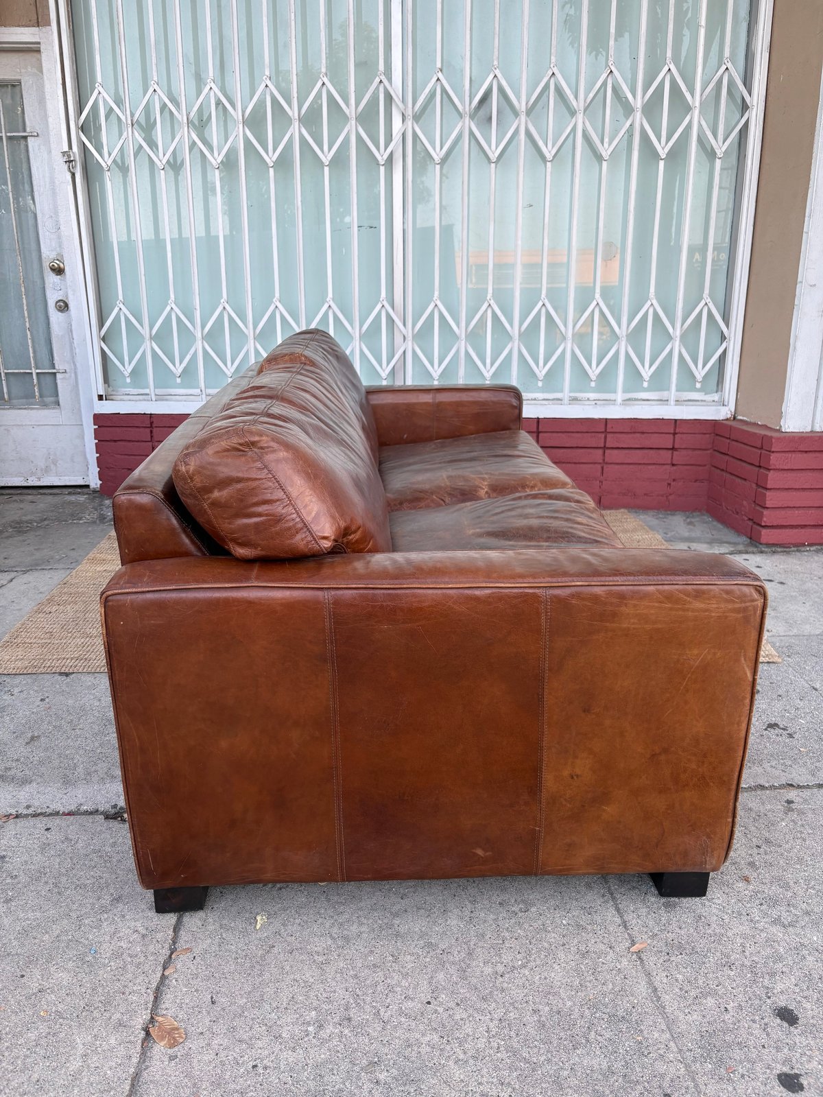 Brown leather sofa with pillow on concrete patio, white metal accordion gate doors in background