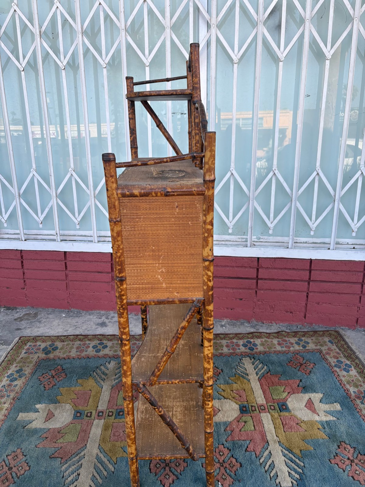 Antique wooden ladder-back chair with woven seat on patterned rug in front of white and red metal door
