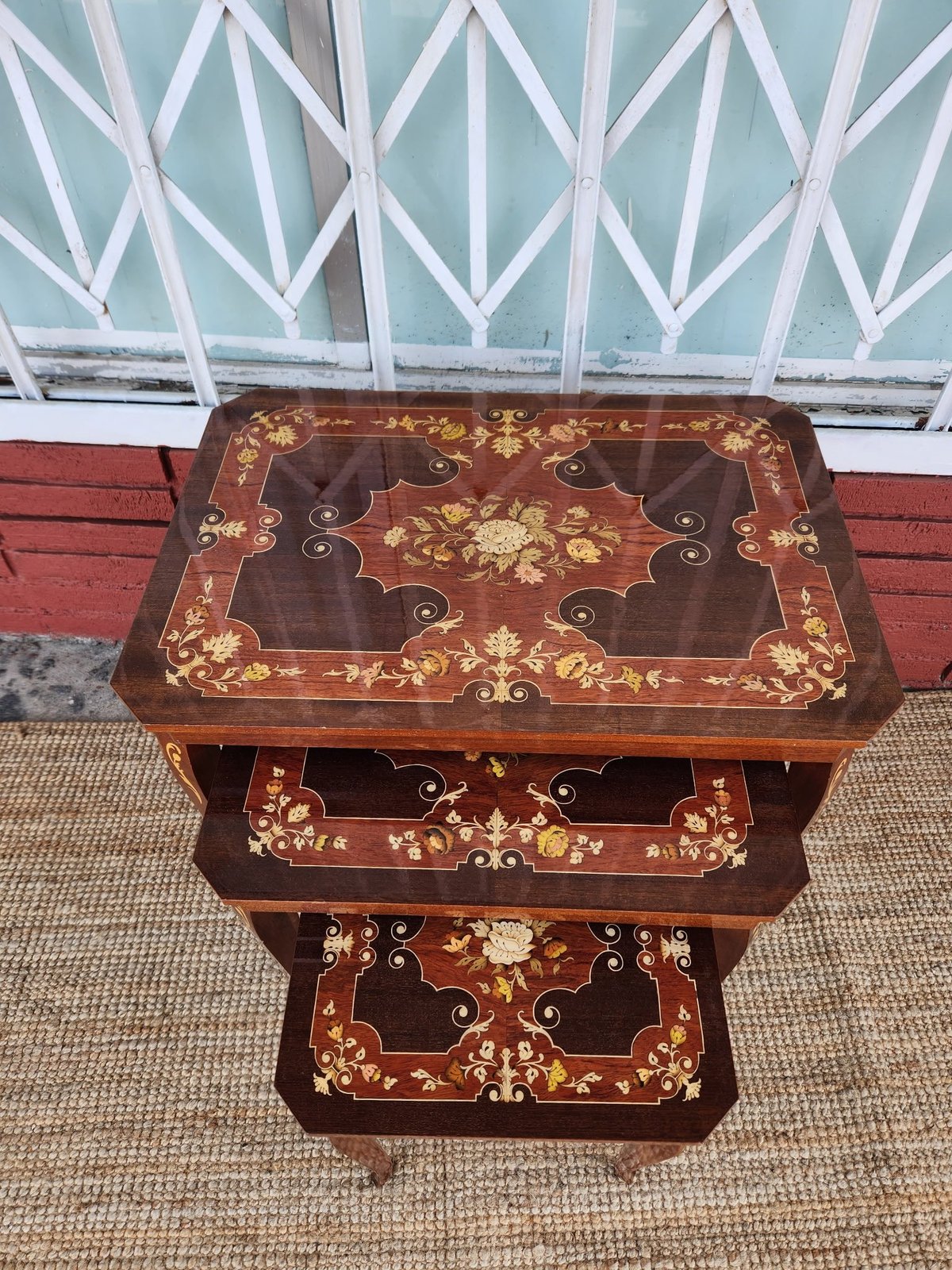 Antique wooden nesting tables with ornate floral inlay designs in gold and brown finish, stacked outdoors on concrete patio