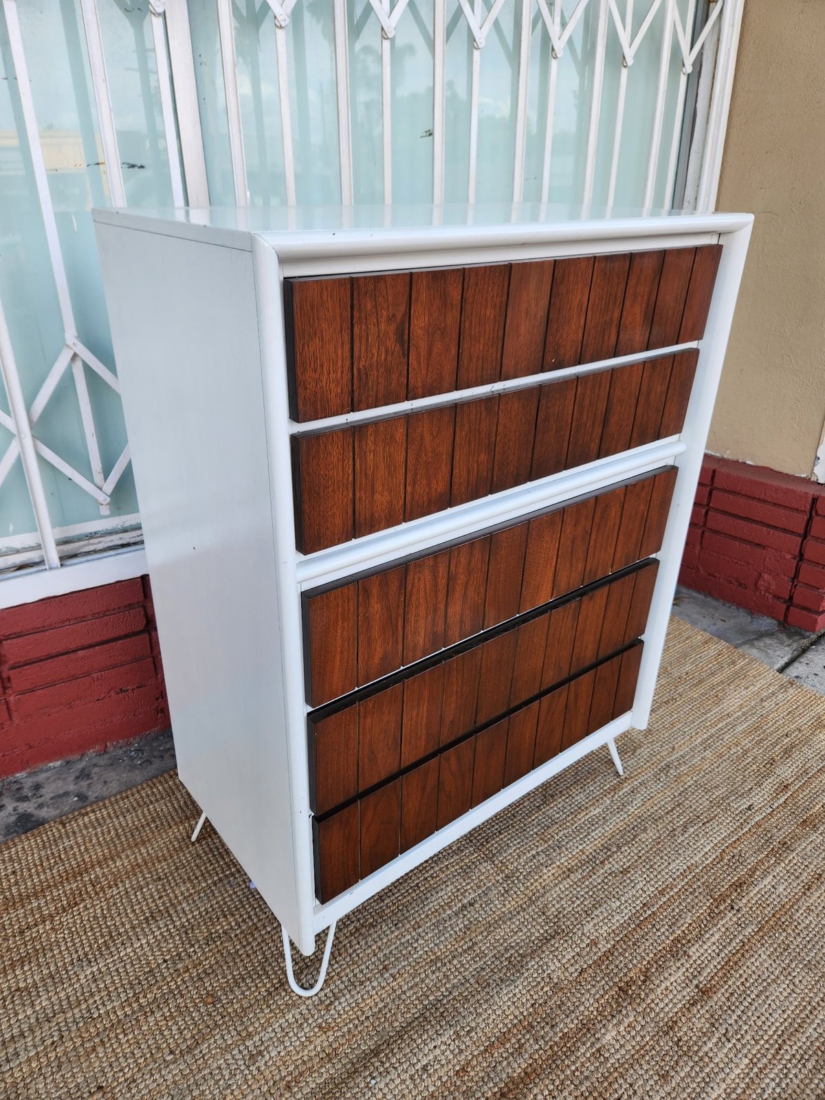 White and wood mid-century modern dresser with five drawers on metal legs in a showroom