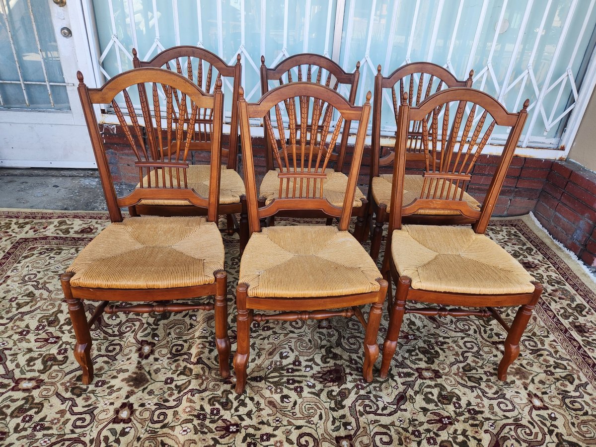 Three wooden dining chairs with woven rush seats and fan-shaped backs arranged on a decorative rug