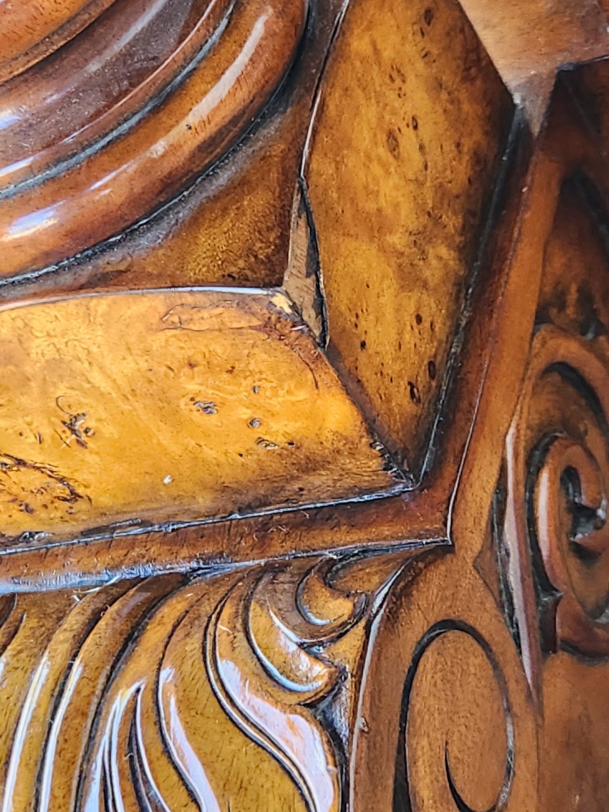 Close-up of intricately carved wooden architectural detail with ornate scrollwork and decorative molding in warm amber tones