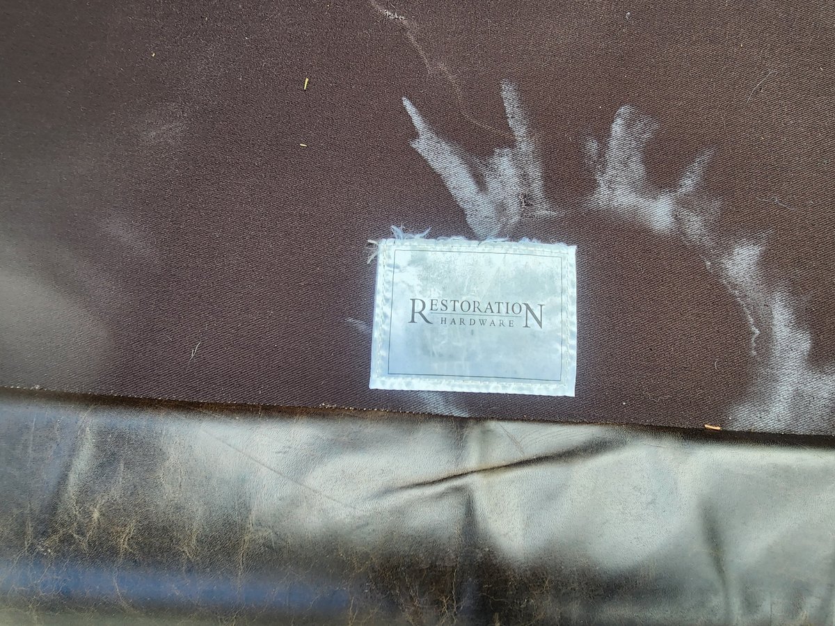 Closeup of a worn fabric label reading Restoration with faded palm frond design on dark textured background