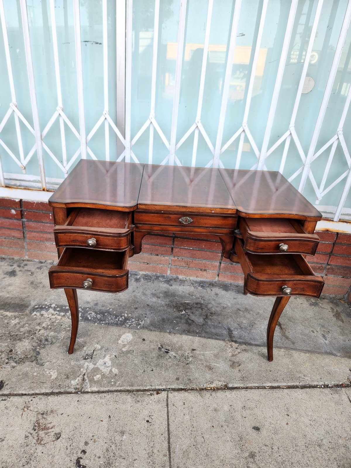 Vintage wooden desk with multiple drawers displayed outside against brick wall and accordion window shade