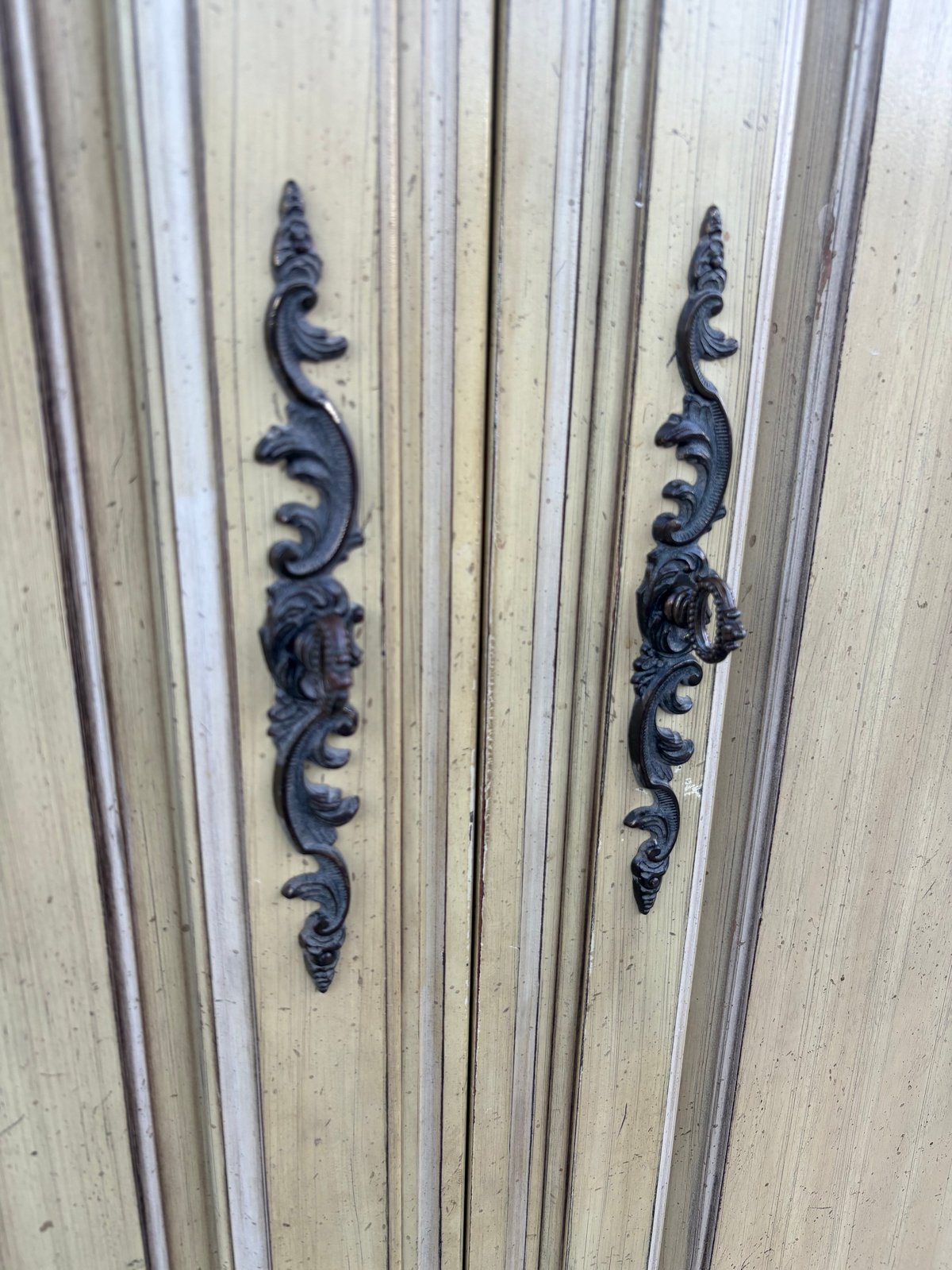 Ornate black metal handles on cream-colored wooden cabinet doors with vertical grooves