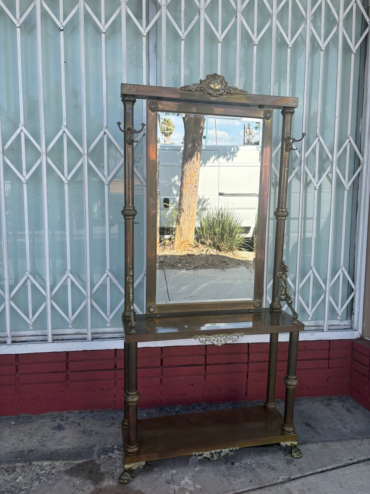 Antique wooden mirror with ornate frame and shelf on casters displayed against corrugated metal wall