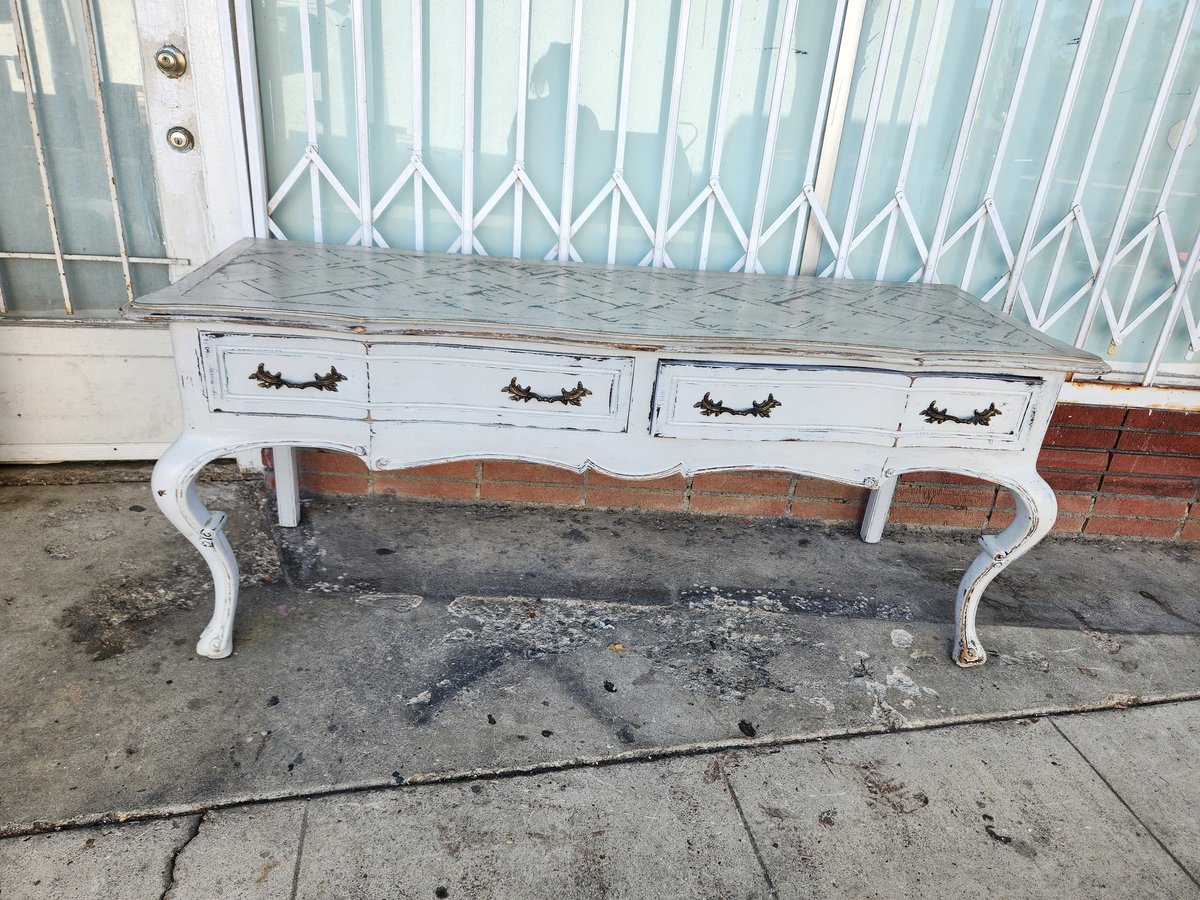 White distressed dresser with four drawers and ornate curved legs sitting on concrete pavement