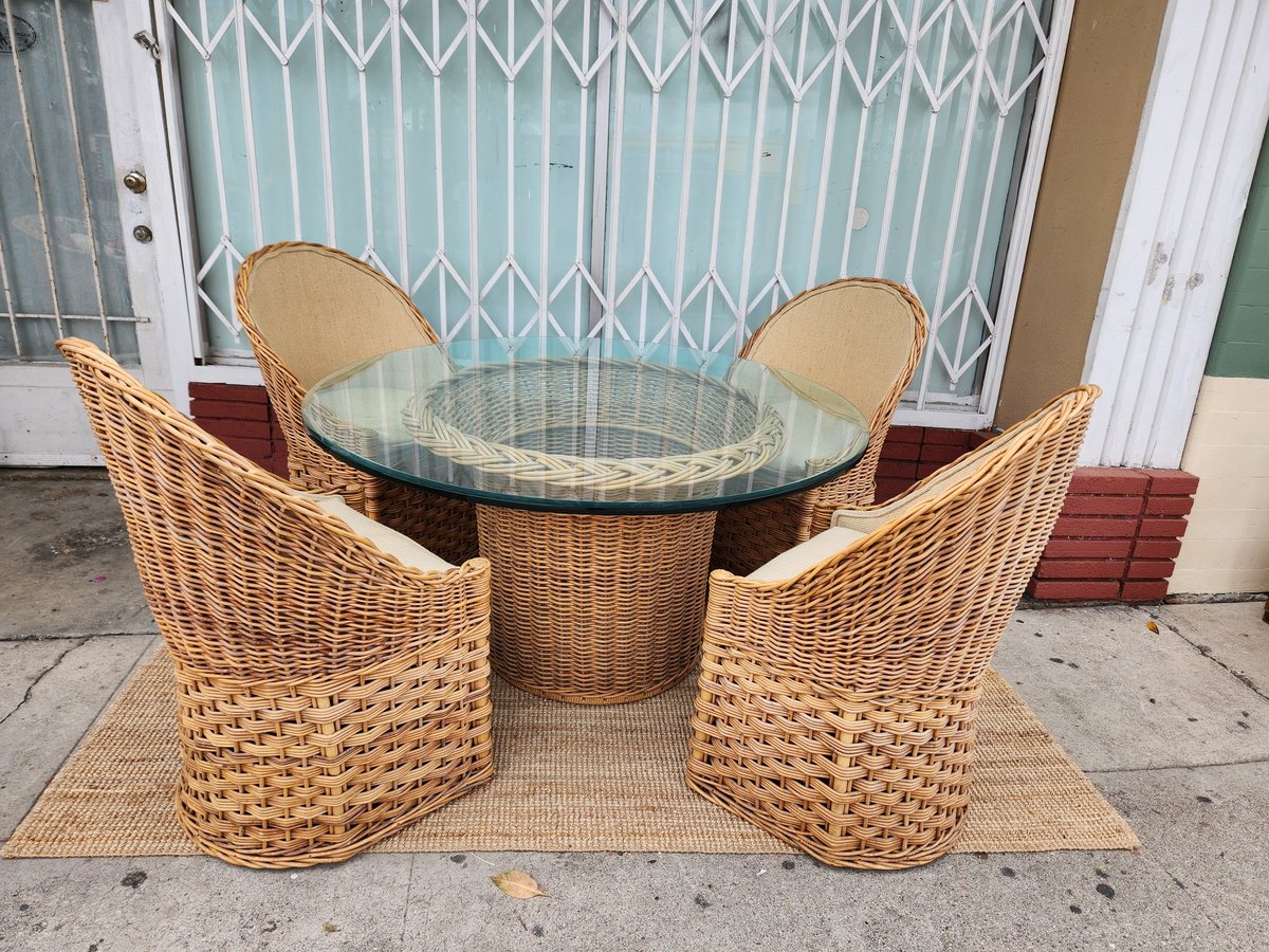 Outdoor patio furniture set with round glass-top table and four woven wicker chairs on concrete floor