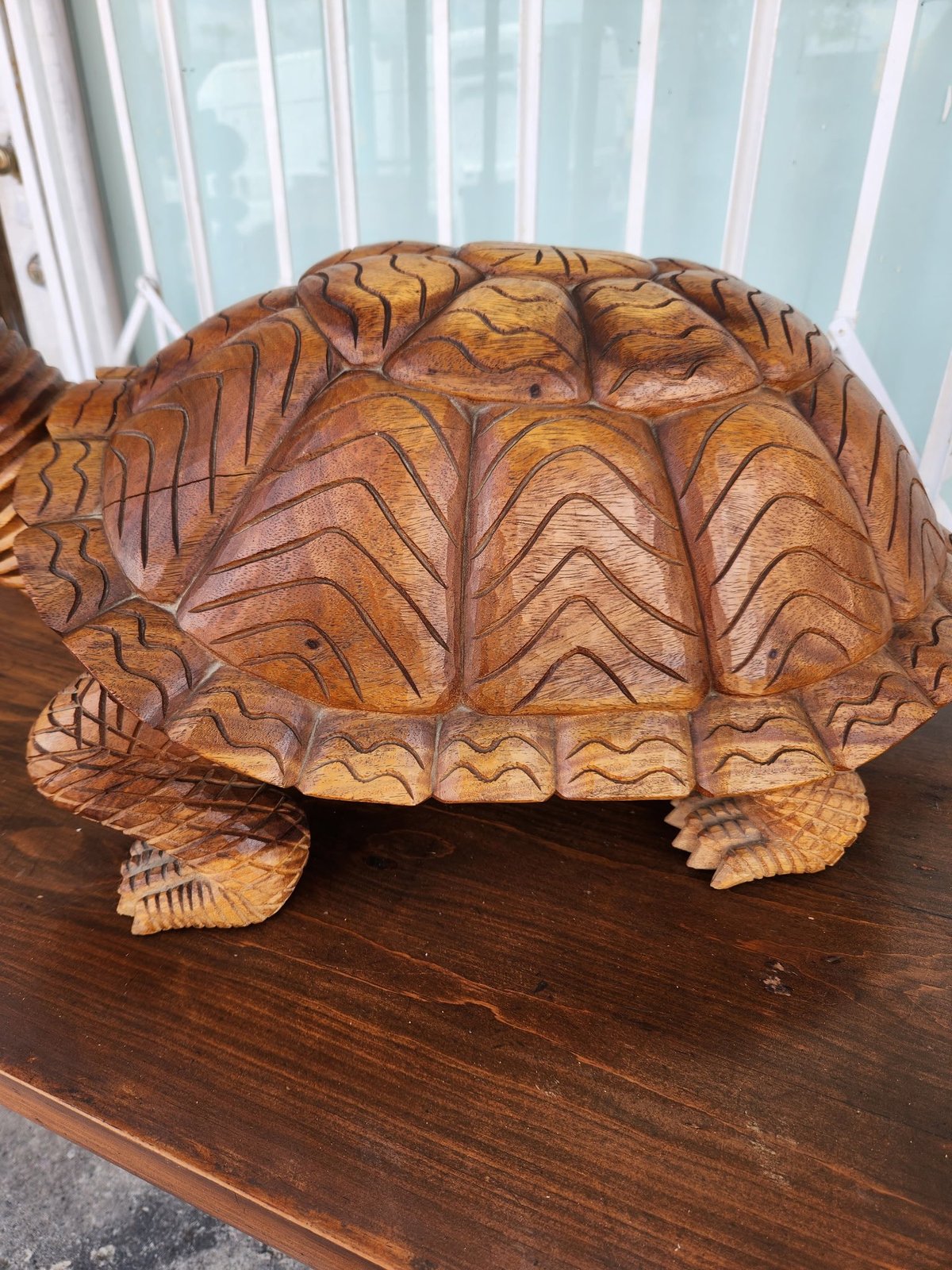 Hand-carved wooden turtle sculpture with intricate shell details on a dark wooden table indoors