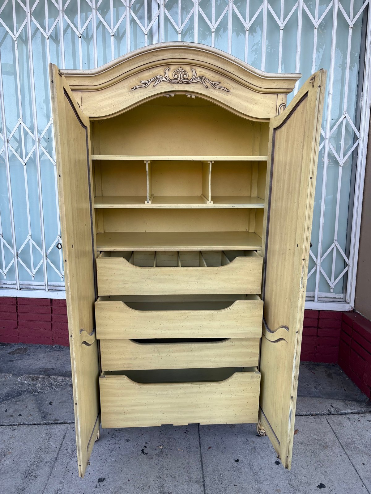 Vintage light wood armoire with curved top, open doors showing shelves and multiple pull-out drawers inside