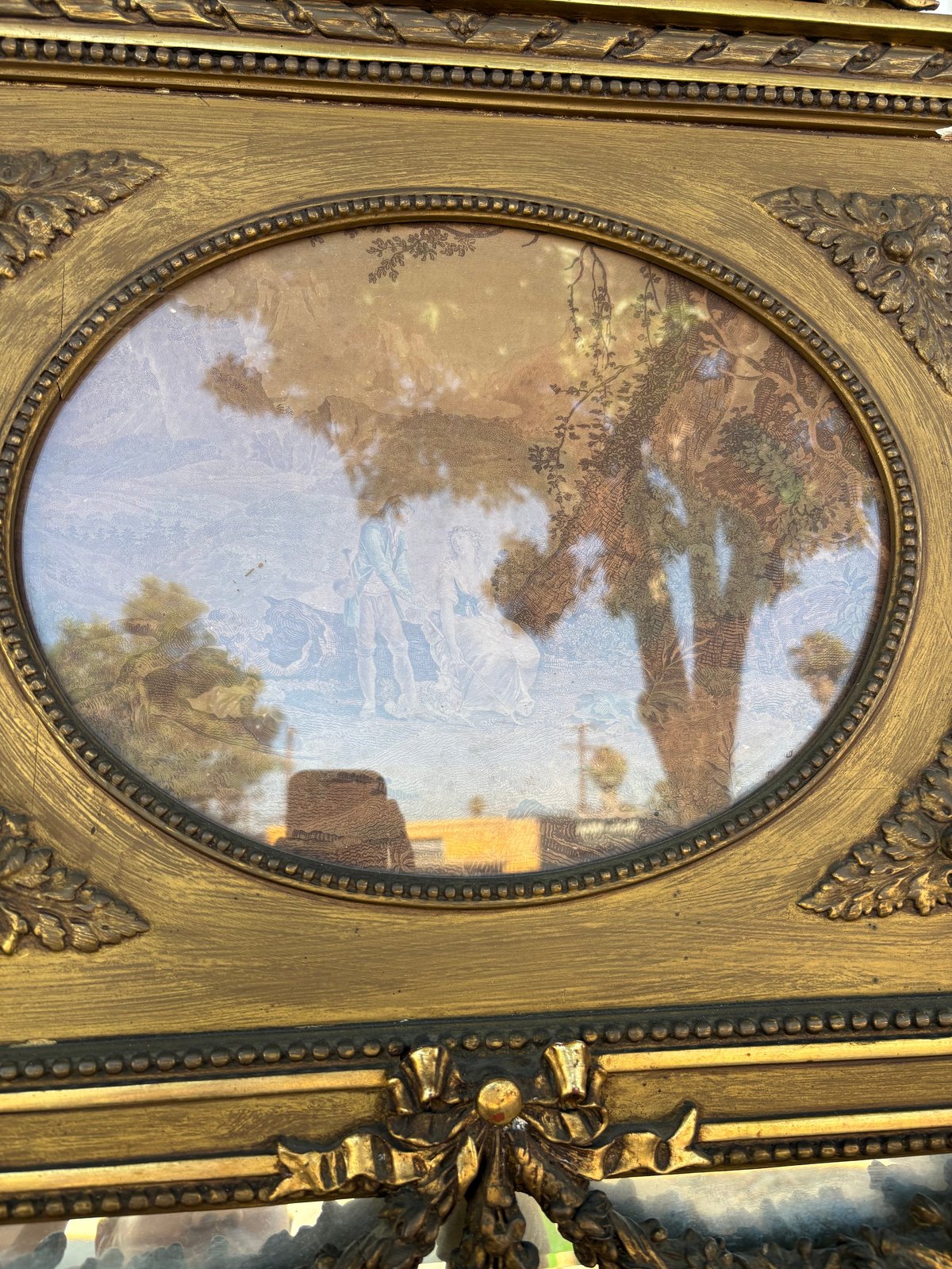 Oval landscape painting in ornate gold frame depicting a rural scene with trees, fields, and a distant structure