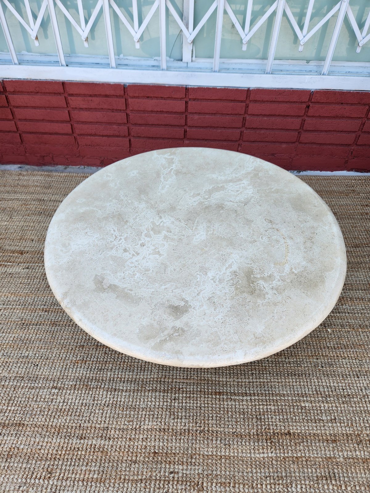 Large white round concrete table on beige carpet with red headboard and white geometric pattern backdrop