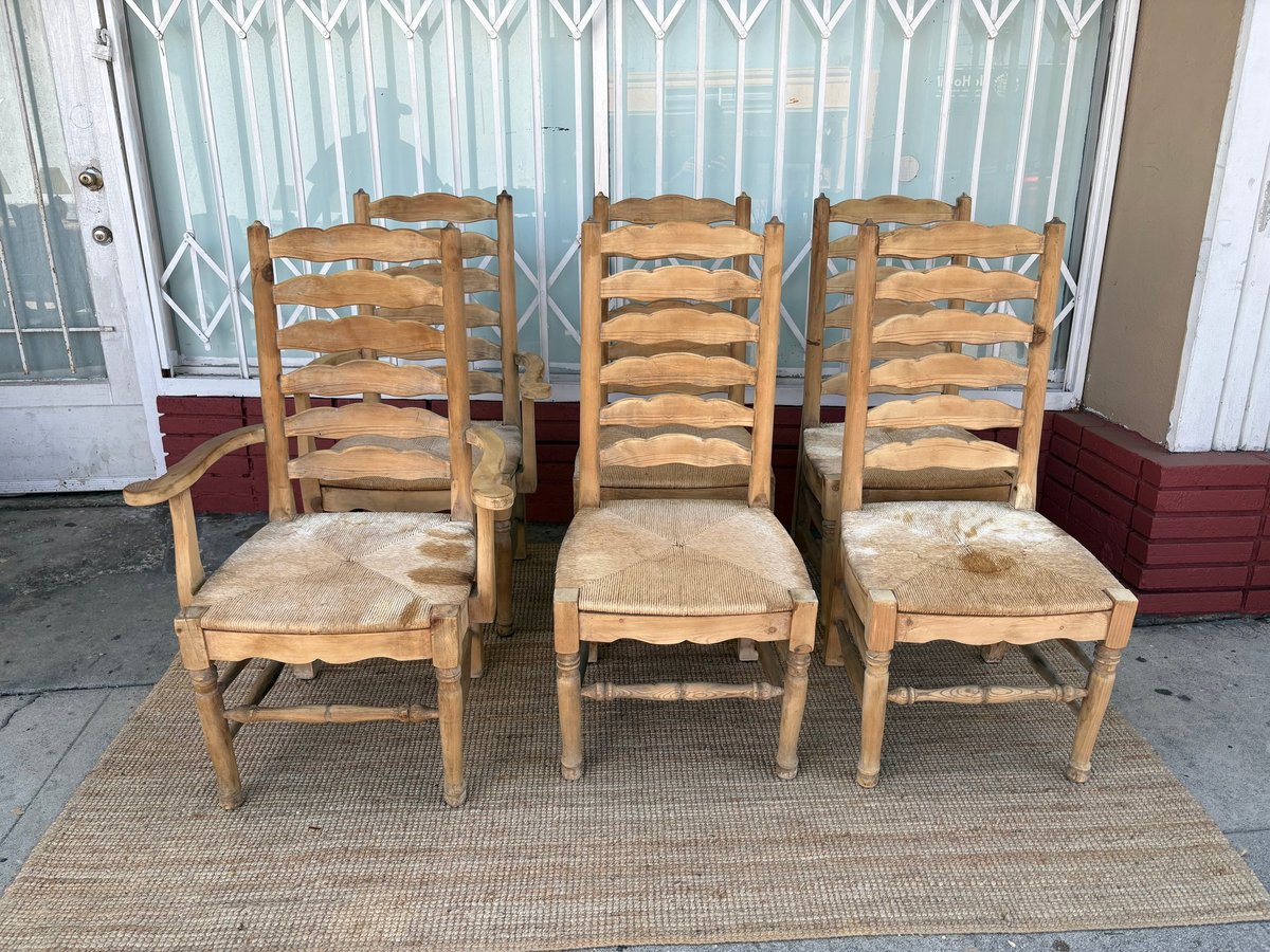 Three wooden ladder-back chairs with woven rush seats arranged on a beige mat outdoors