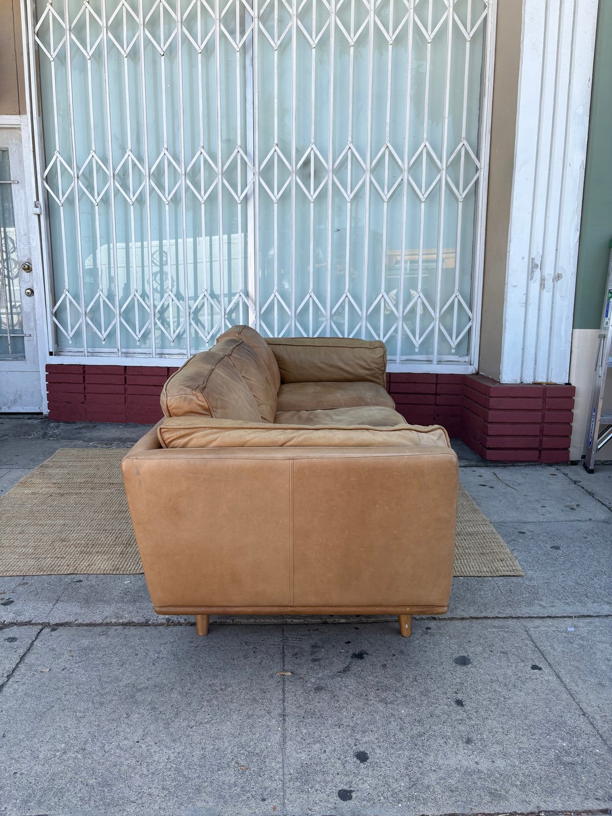 Tan leather armchair on sidewalk in front of storefront with metal security gates and red brick planter