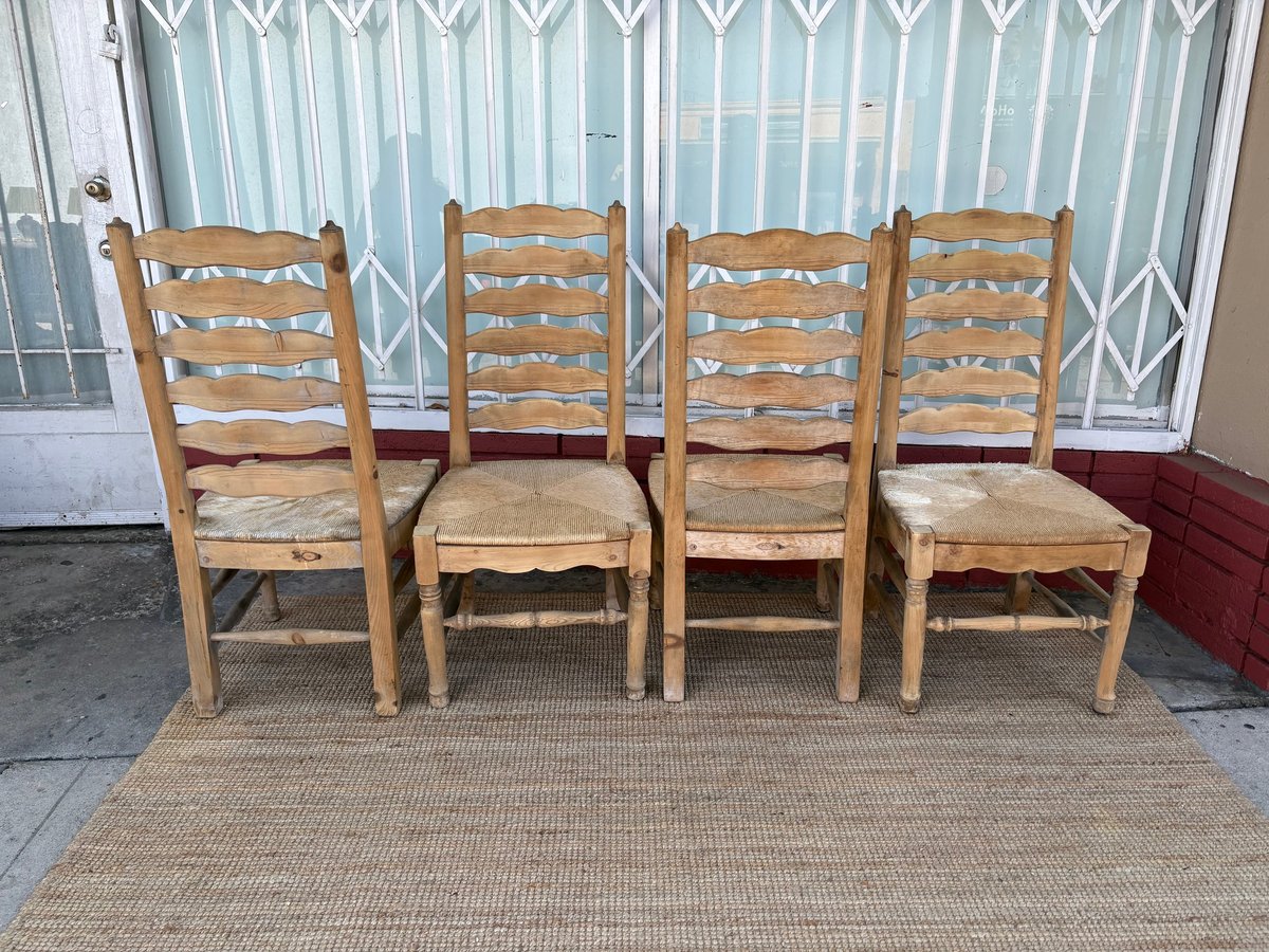 Four wooden ladder-back chairs with woven rush seats arranged on a beige mat in front of a window