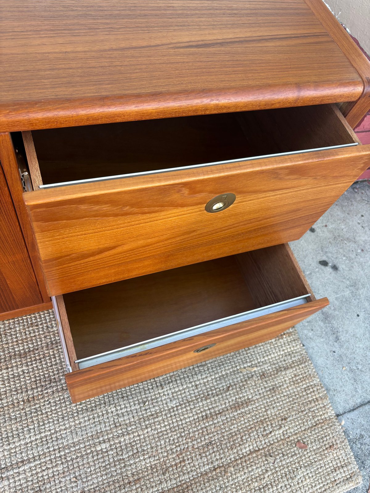 Wooden dresser with two open drawers showing interior compartments, placed on a concrete surface