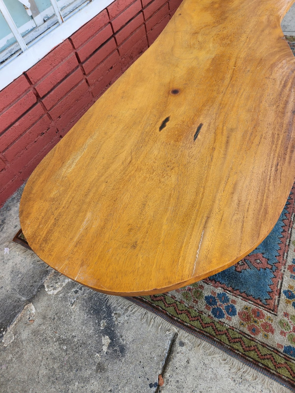 Overhead view of an oval-shaped wooden table with honey-toned finish on concrete floor next to red brick wall