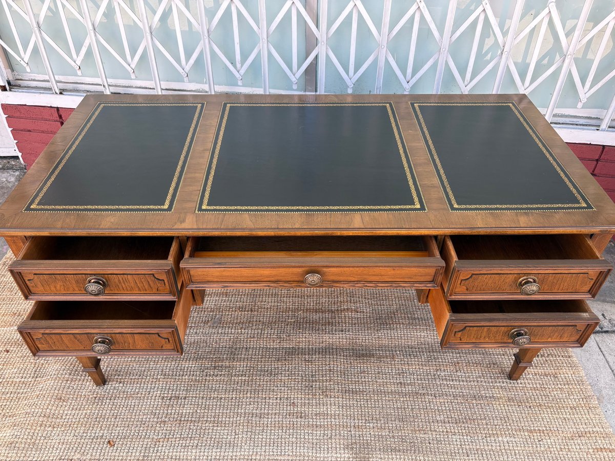 Wooden desk with three dark leather inlaid surfaces, four drawers, and tapered legs on a beige rug