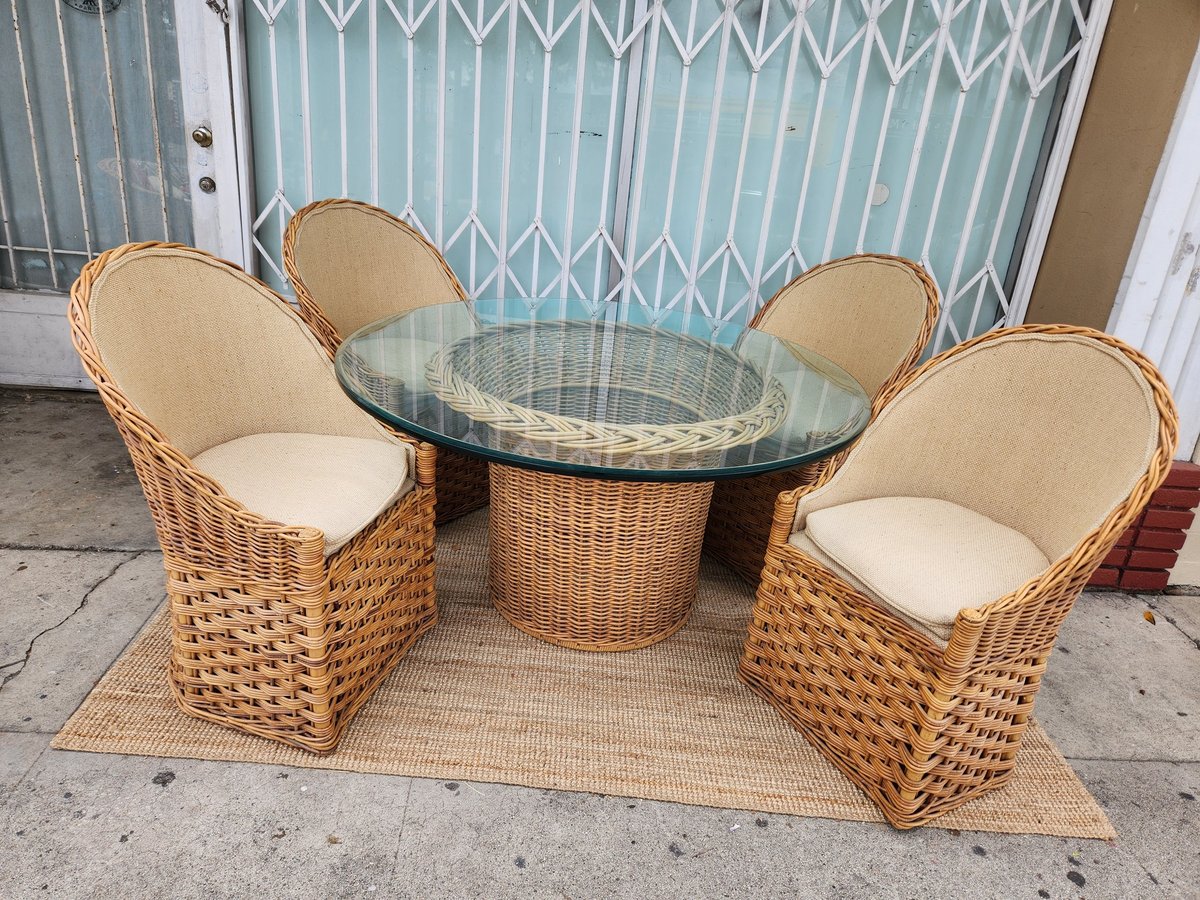 Wicker patio furniture set with round glass-top table and four cushioned chairs on a woven rug