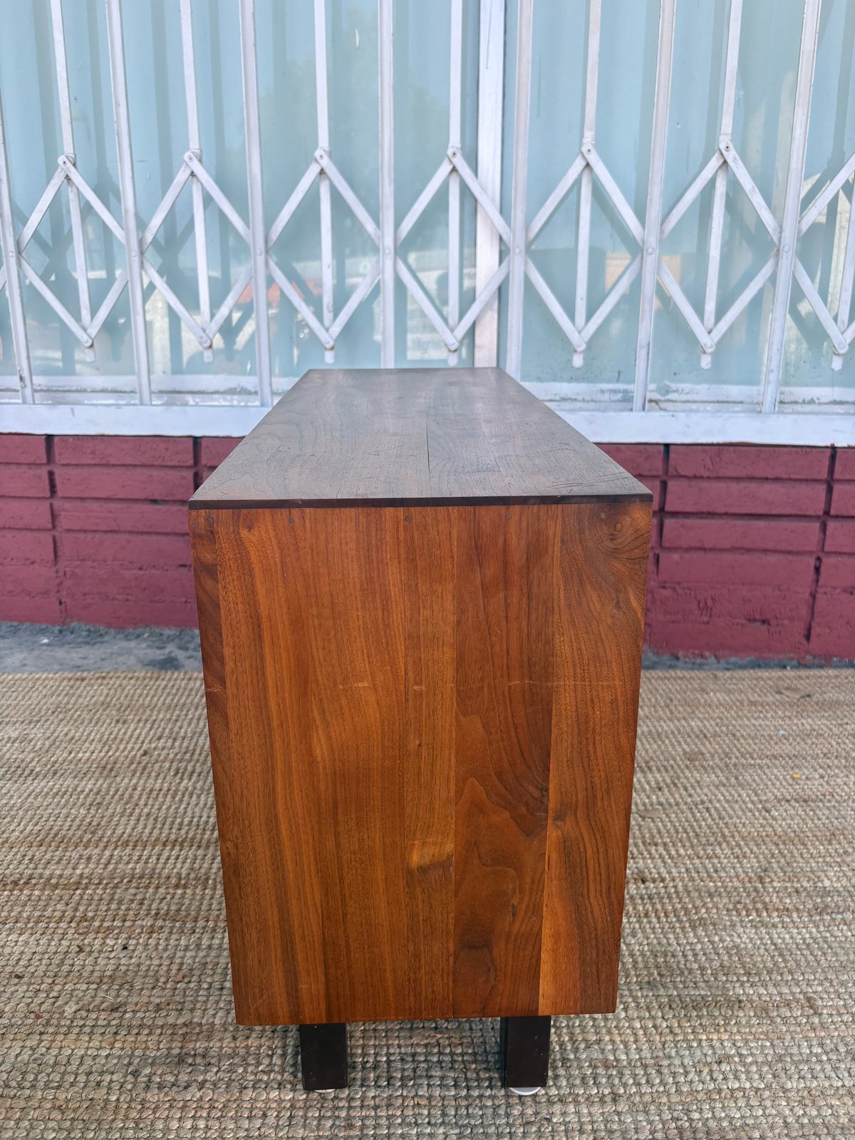 Wooden storage chest with gray top and black legs against red brick wall and metal gate backdrop