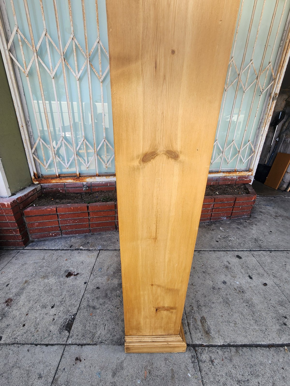 Tall wooden board leaning against blue latticed window with red brick base in front of building