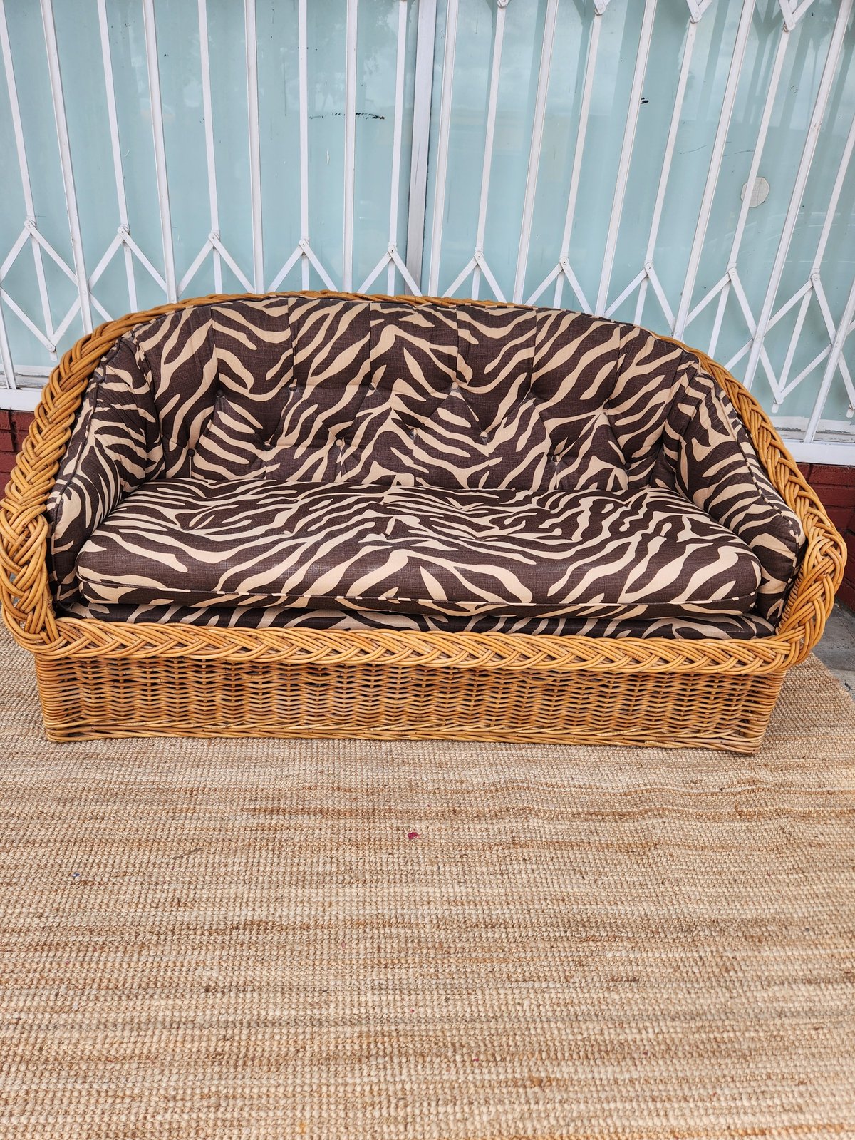 Woven wicker sofa with zebra stripe cushions against a geometric patterned wall