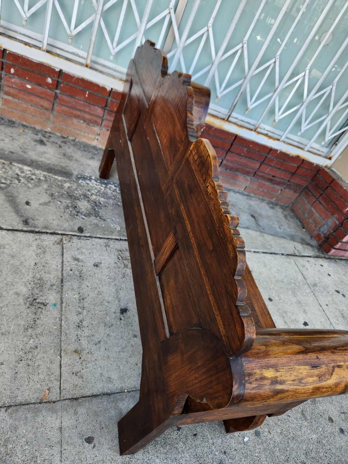 Dark wooden rocking chair displayed upside down on outdoor pavement with brick wall and metal roof background