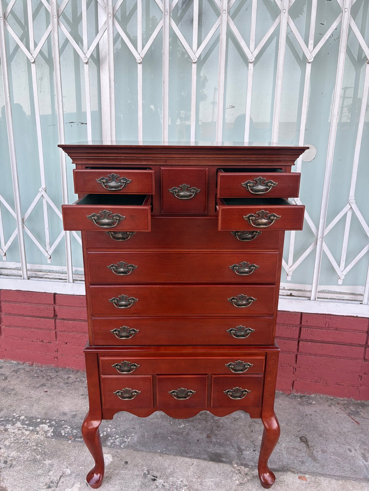 Red wooden dresser with multiple drawers and metal handles against a white latticed door background.
